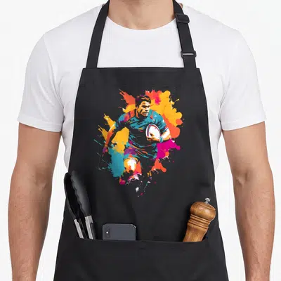 Tablier de cuisine noir avec illustration colorée d'un joueur de rugby tenant la balle sur fond d'éclaboussures artistiques.