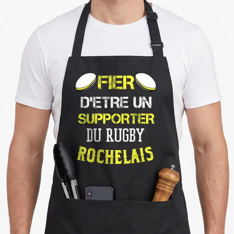Tablier de cuisine noir avec l'inscription FIER D'ETRE UN SUPPORTER DU RUGBY ROCHELAIS et deux ballons de rugby jaunes.