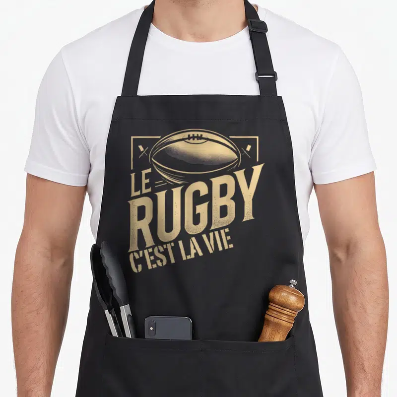 Tablier de cuisine noir avec illustration vintage d'un ballon ovale et le texte Le Rugby C'est la vie en lettres dorées.