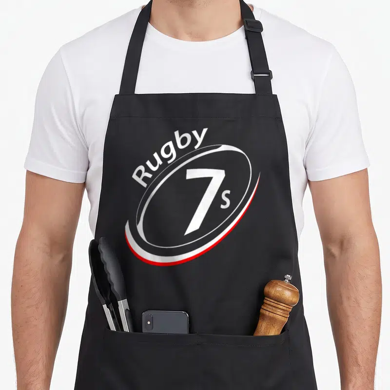 Tablier de cuisine noir avec un logo ovale blanc et rouge portant l'inscription Rugby 7s au centre.