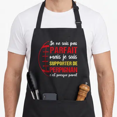 Tablier de cuisine noir avec texte blanc et rouge supporteur de perpignan et illustration de ballon de rugby sur fond uni.