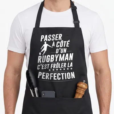 Tablier de cuisine noir avec une silhouette blanche de joueur de rugby et le texte blanc passant à côté d'un rugbyman c'est frôler la perfection.
