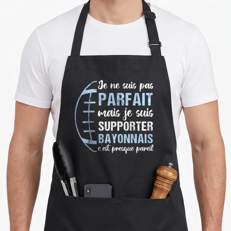 Tablier de cuisine noir avec dessin de ballon de rugby et texte blanc et bleu clair sur fond gris uni