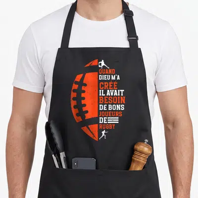 Tablier de cuisine noir avec une balle de rugby orange et le texte quand dieu m'a cree il avait besoin de bons joueurs de rugby en blanc et orange.