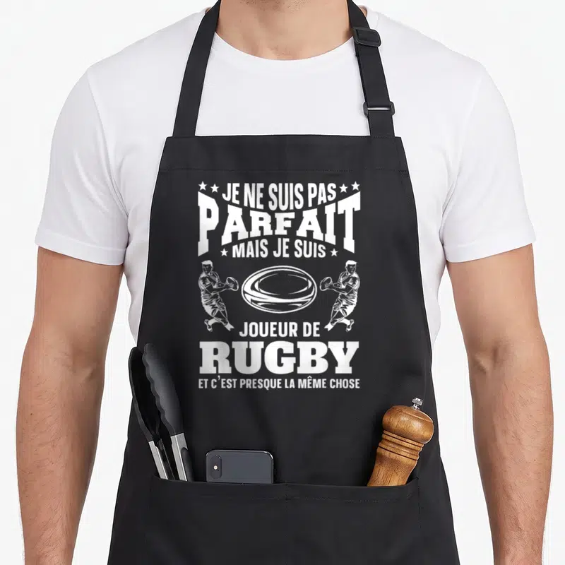 Tablier de cuisine noir avec inscription blanche Je ne suis pas parfait joueur de rugby et deux joueurs tenant un ballon.