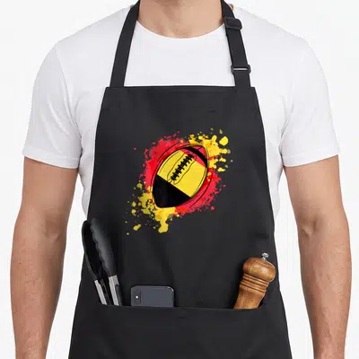 Tablier de cuisine noir avec ballon de rugby aux couleurs belges et éclaboussures rouges et jaunes.
