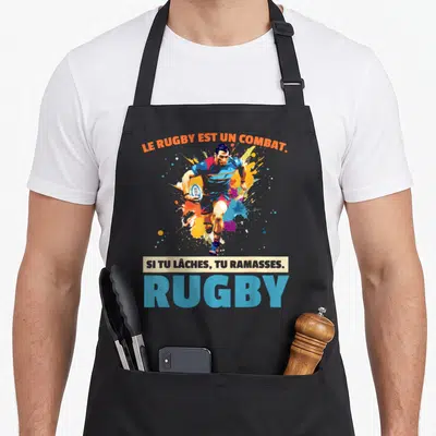 Tablier de cuisine noir avec joueur de rugby en action et texte humoristique sur fond d'éclaboussures colorées.