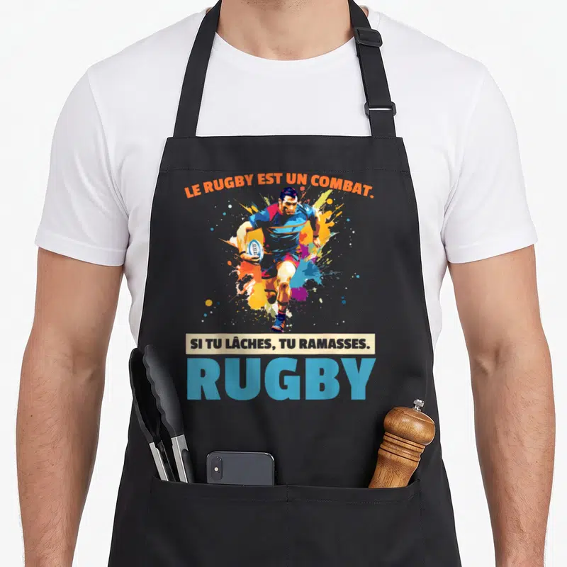 Tablier de cuisine noir avec joueur de rugby en action et texte humoristique sur fond d'éclaboussures colorées.