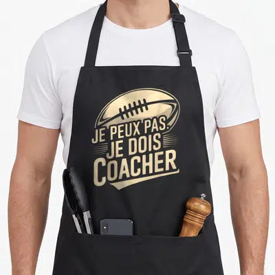 Tablier de cuisine noir avec illustration de ballon de rugby et texte Je peux pas je dois coacher en beige vintage.