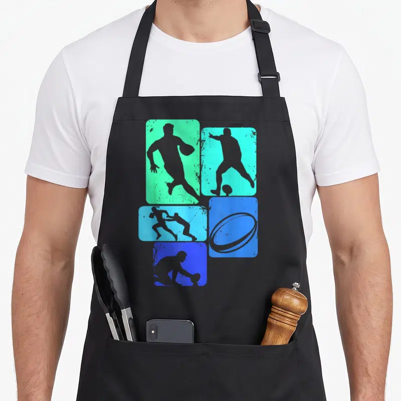 Tablier de cuisine noir avec silhouettes de joueurs de rugby et ballon ovale sur fonds colorés dégradés.