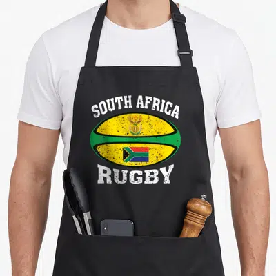 Tablier de cuisine noir avec un ballon de rugby jaune et vert portant les mots South Africa Rugby et le drapeau national.