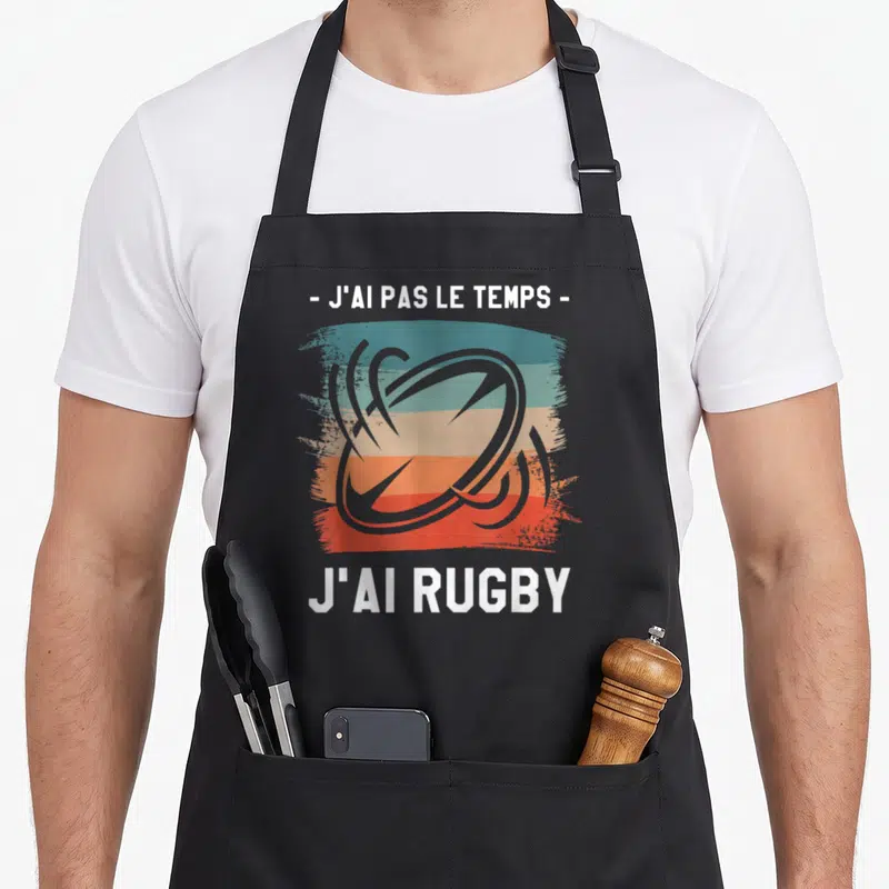 Tablier de cuisine noir avec illustration d'un ballon de rugby et texte blanc sur bandes colorées.