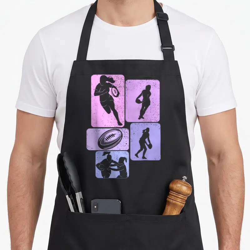 Tablier de cuisine noir avec silhouettes de joueuses de rugby et ballon ovale sur fonds rose et violet texturés.