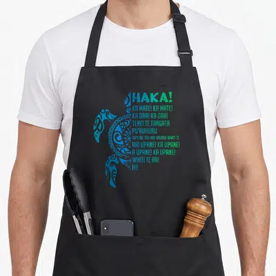 Tablier de cuisine noir avec une tortue bleue stylisée et le texte Haka Ka Mate en vert et bleu.