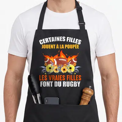 Tablier de cuisine noir avec des ballons de rugby en feu et des fleurs jaunes sous le texte imprimé.