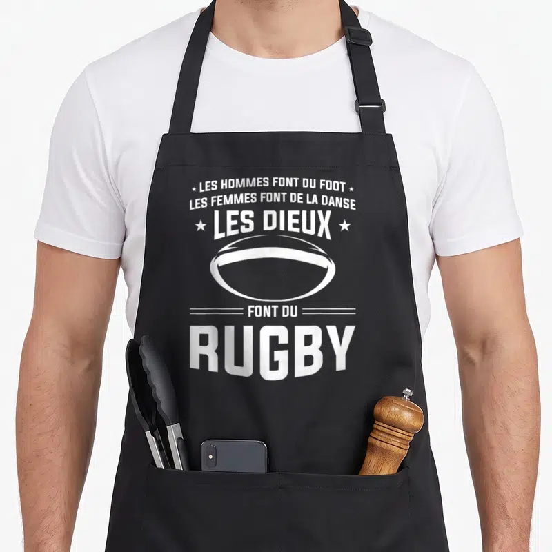 Tablier de cuisine noir avec inscription blanche Les Dieux Font Du Rugby et dessin d'un ballon ovale au centre.