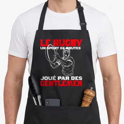 Tablier de cuisine noir avec illustration d'un joueur de rugby tenant un ballon et texte en blanc et rouge.