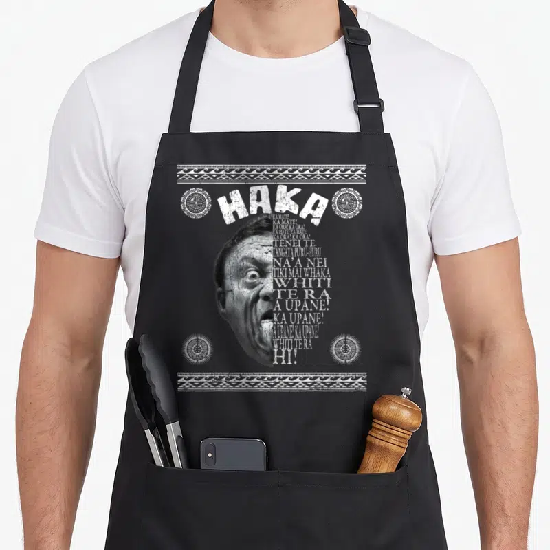 Tablier de cuisine noir avec illustration Haka guerrier Maori et motifs tribaux blancs en haut et en bas.