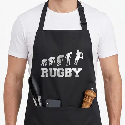 Tablier de cuisine noir avec silhouette évolutive d'un joueur de rugby et le mot RUGBY en lettres capitales texturées.