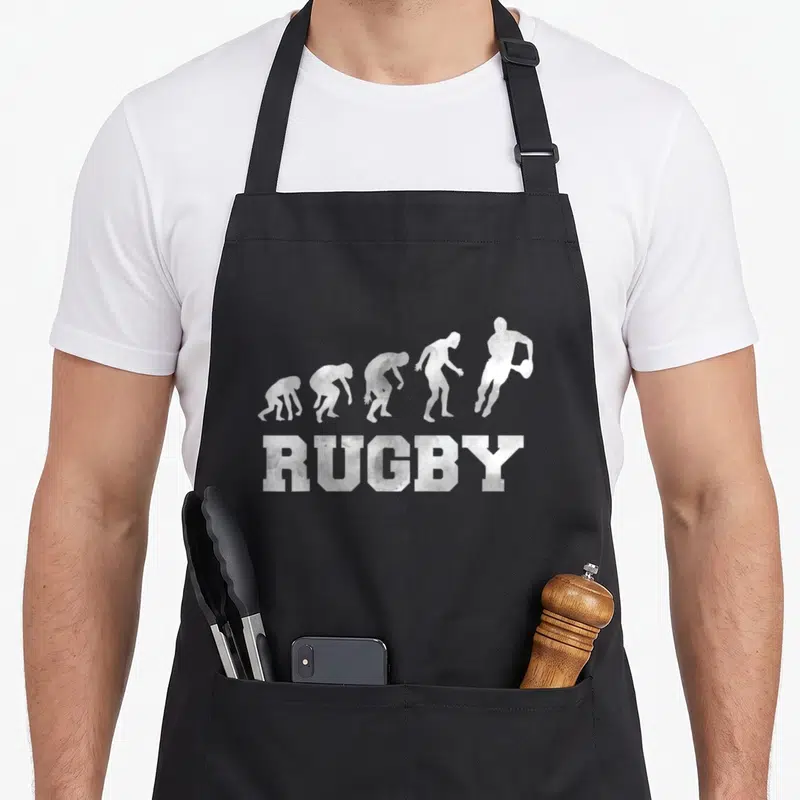 Tablier de cuisine noir avec silhouette évolutive d'un joueur de rugby et le mot RUGBY en lettres capitales texturées.