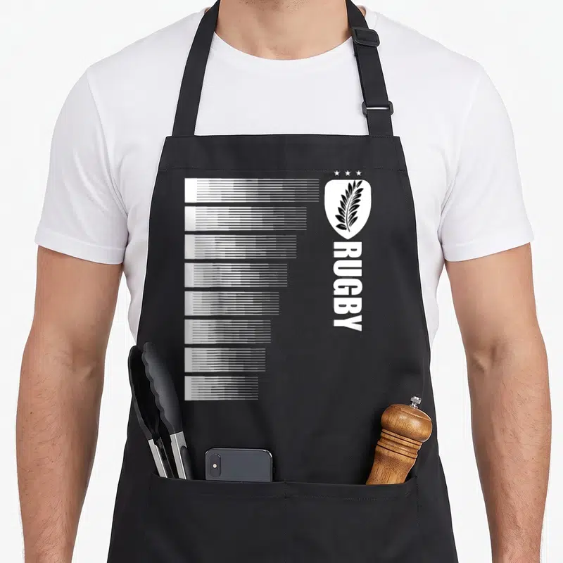 Tablier de cuisine noir avec motif blanc vertical imitant des rayures de maillot et un insigne à la feuille d'argent surmonté de trois étoiles.