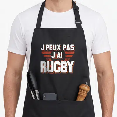 Tablier de cuisine noir avec inscription J'peux pas j'ai rugby en blanc et orange stylisé.