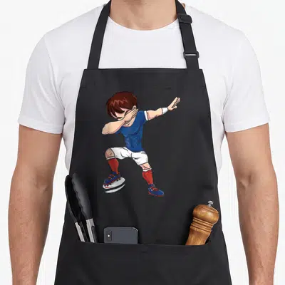 Tablier de cuisine noir avec illustration d'un joueur de rugby en tenue bleue faisant une pose dab sur un ballon blanc.