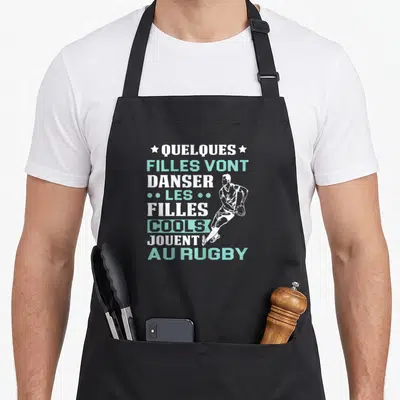 Tablier de cuisine noir avec inscription blanche et turquoise sur le rugby et silhouette d'une joueuse en mouvement.