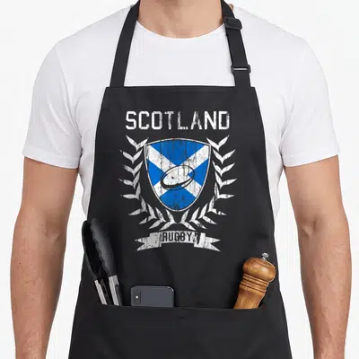 Tablier de cuisine noir avec un blason écossais bleu et blanc encadré de lauriers blancs et le texte SCOTLAND RUGBY en haut et en bas.