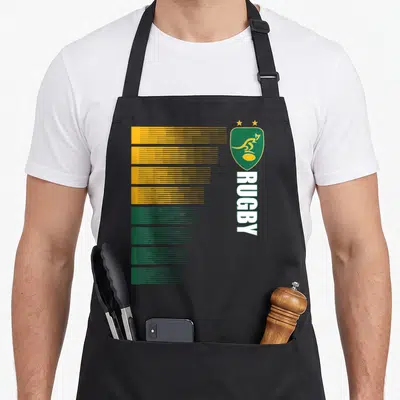 Tablier de cuisine noir avec un motif graphique vert et jaune représentant un écusson de rugby australien et le texte RUGBY vertical.