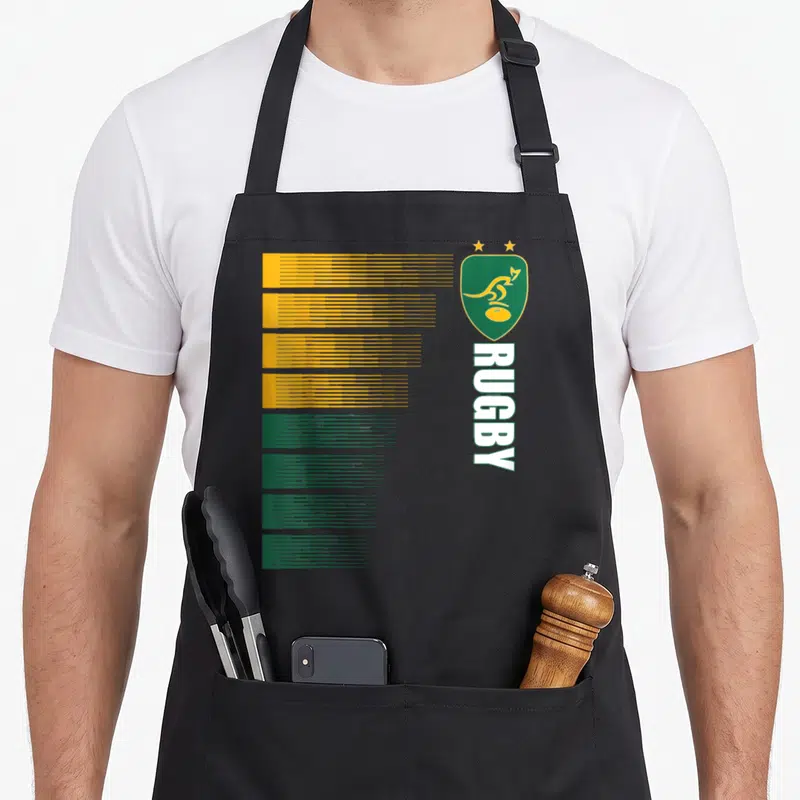 Tablier de cuisine noir avec un motif graphique vert et jaune représentant un écusson de rugby australien et le texte RUGBY vertical.