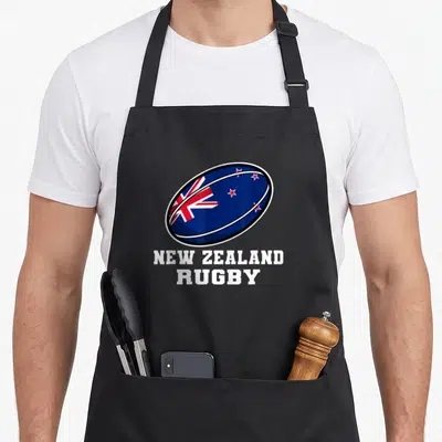 Tablier de cuisine noir avec un ballon de rugby bleu portant l'inscription NEW ZEALAND RUGBY en lettres blanches.