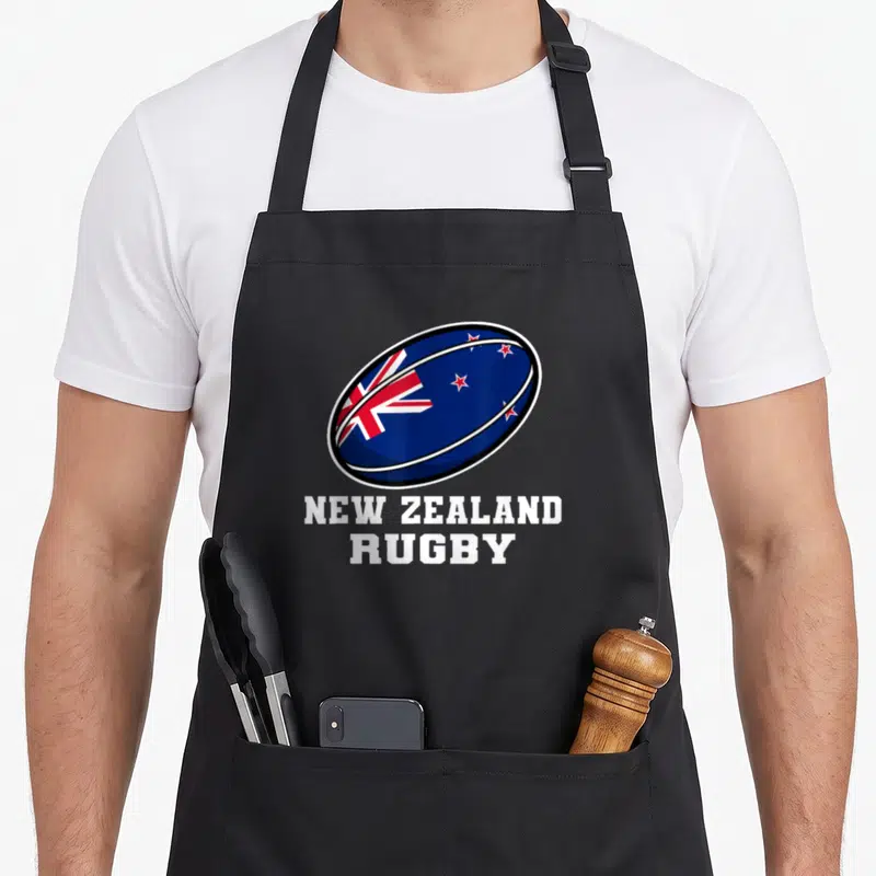 Tablier de cuisine noir avec un ballon de rugby bleu portant l'inscription NEW ZEALAND RUGBY en lettres blanches.