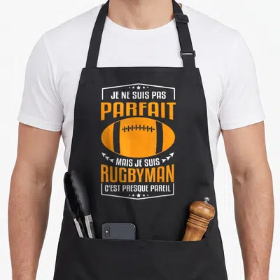 Tablier de cuisine noir avec inscription Je ne suis pas parfait mais je suis rugbyman et ballon orange stylisé.