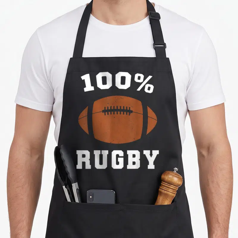 Tablier de cuisine noir avec un ballon de rugby orange et l'inscription 100% Rugby en blanc.