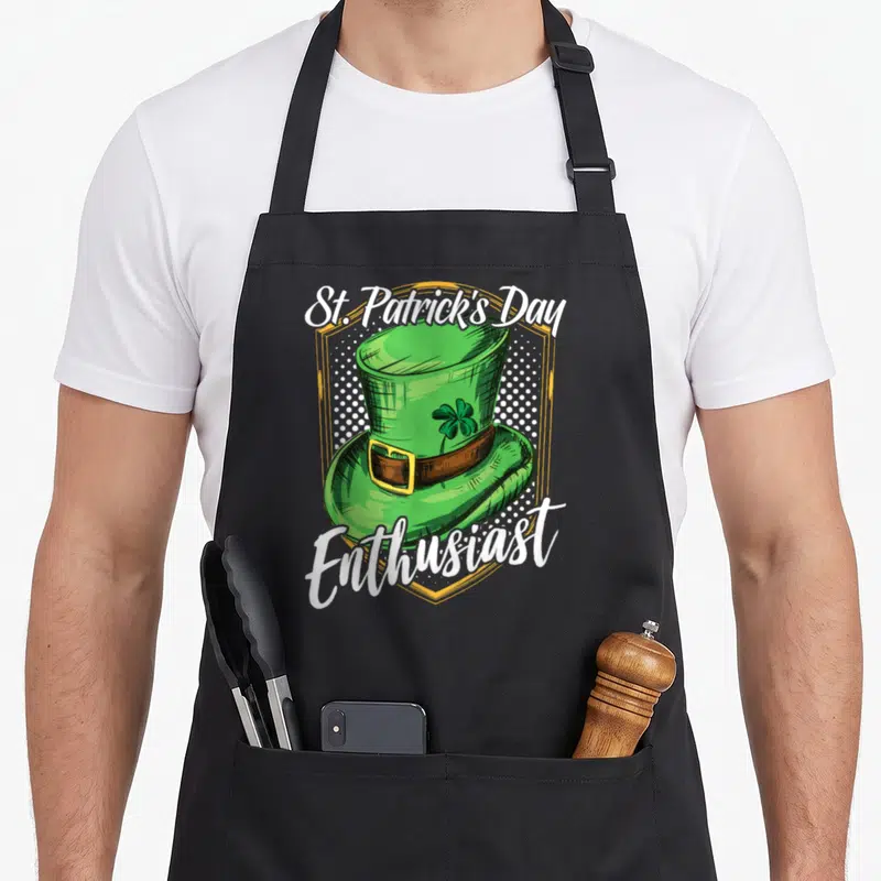 Tablier de cuisine noir avec illustration chapeau vert trèfle et texte St. Patrick's Day Enthusiast encadré d'or.