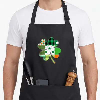 Tablier de cuisine noir avec un grand trèfle multicolore en motif patchwork vert orange et blanc.