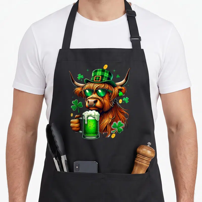 Tablier de cuisine noir avec une vache des Highlands portant un chapeau vert et tenant une bière verte.
