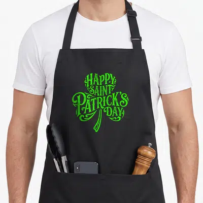 Tablier de cuisine noir avec un grand trèfle vert formé par du texte festif.