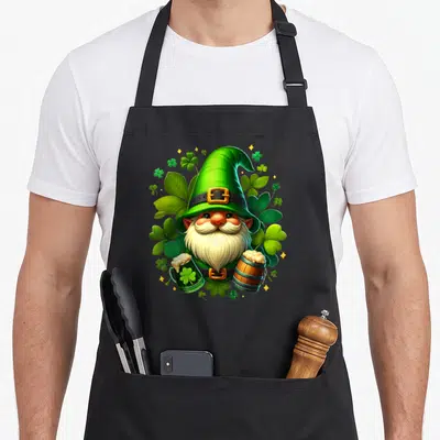 Tablier de cuisine noir avec un gnome vert coiffé d'un chapeau pointu tenant deux verres de bière au milieu de trèfles.
