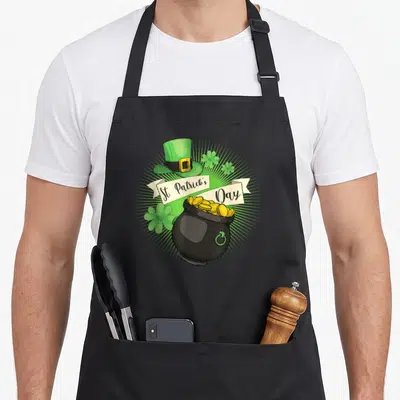 Tablier de cuisine noir avec illustration d'un chapeau vert, d'un pot de pièces d'or et de trèfles pour la Saint-Patrick.
