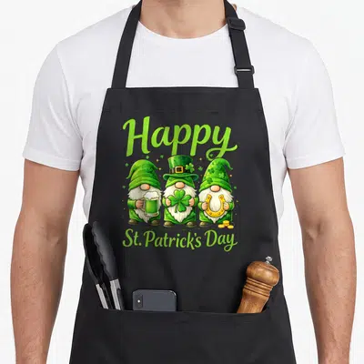 Tablier de cuisine noir avec trois gnomes verts, bière, trèfle, fer à cheval et texte Happy St. Patrick's Day en vert.