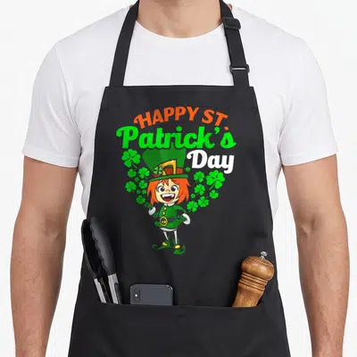 Tablier de cuisine noir avec une illustration colorée d'une leprechaun fille et des trèfles verts sur fond uni.