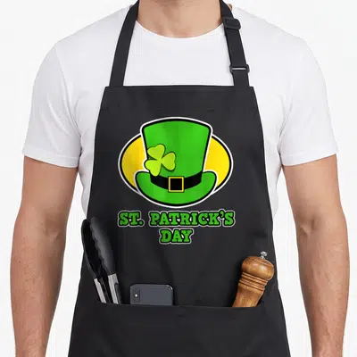 Tablier de cuisine noir avec un chapeau vert, un trèfle et l'inscription St. Patrick's Day en lettres vertes.