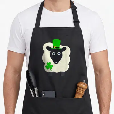 Tablier de cuisine noir avec un mouton blanc portant un chapeau haut de forme vert et tenant un trèfle.