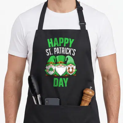 Tablier de cuisine noir avec trois nains verts coiffés de chapeaux pointus tenant un trèfle et un fer à cheval sous l'inscription Happy St Patrick's Day.