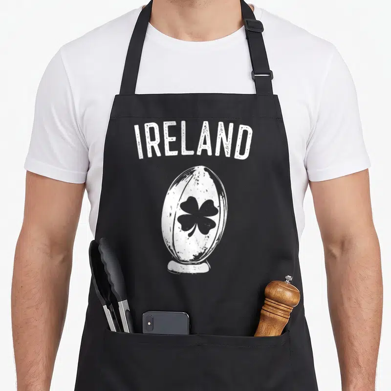 Tablier de cuisine noir avec l'inscription IRELAND et un ballon de rugby orné d'un trèfle noir en style vintage.