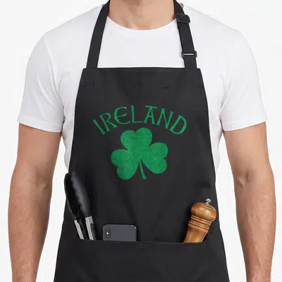 Tablier de cuisine noir avec inscription IRELAND et trèfle vert délavé au centre du torse.