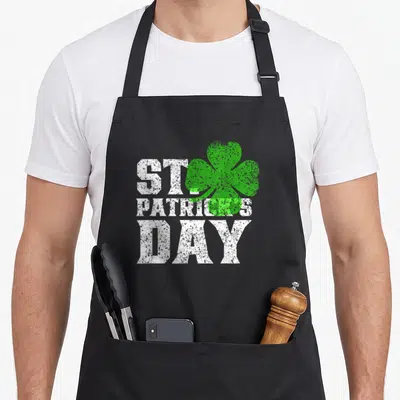 Tablier de cuisine noir avec inscription St Patrick Day blanche et trèfle vert à trois feuilles sur le devant.