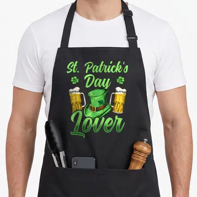 Tablier de cuisine noir avec illustration d'un chapeau vert, deux verres de bière et texte St. Amateur de Saint-Patrick en vert clair.